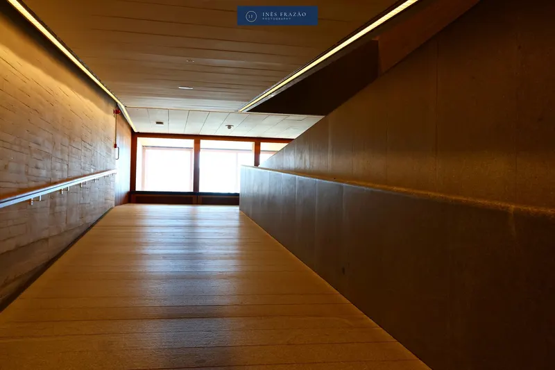 Corredor revestido a madeira com uma janela ao fundo e luz natural, fotografia de arquitetura de interiores por Inês Frazão.
