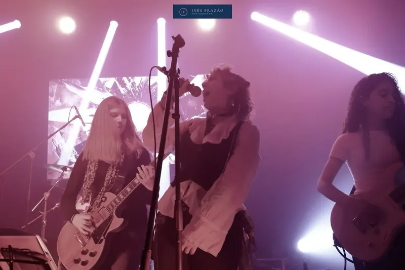 Banda a atuar em palco sob luzes cor-de-rosa e roxas, fotografia de concerto por Inês Frazão.