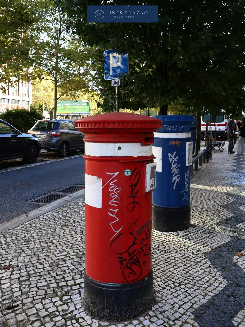 Marcos do correio vermelho e azul num passeio de calçada portuguesa, fotografia de paisagem urbana por Inês Frazão.
