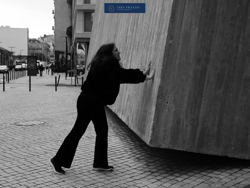 Mulher encostada a um muro de betão numa rua da cidade, a preto e branco, fotografia de retrato urbano por Inês Frazão.