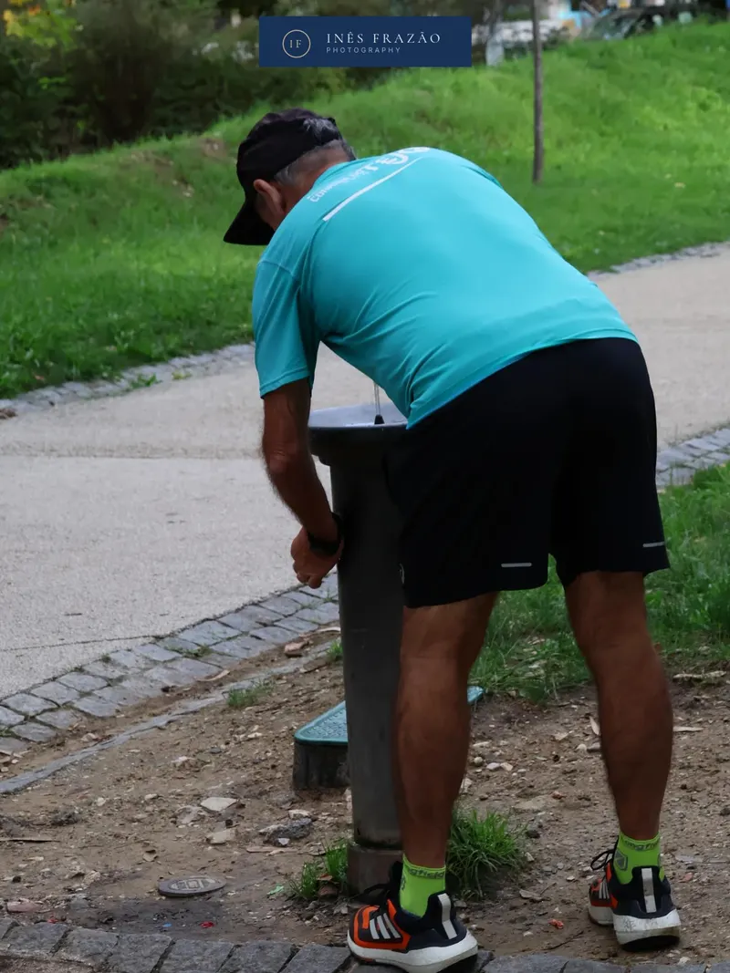Homem a beber água num bebedouro de parque, retrato documental urbano por Inês Frazão.