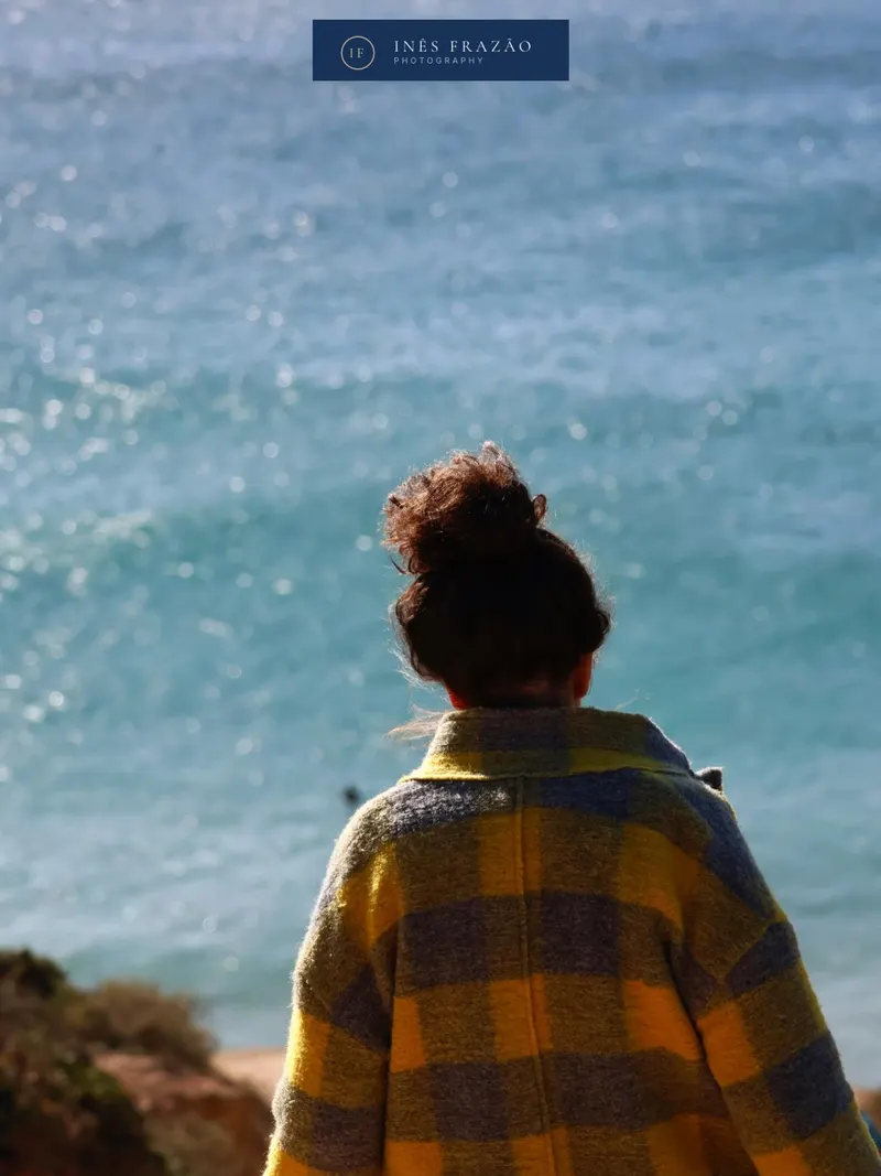 Retrato de costas de uma jovem a observar o mar, numa composição íntima e serena iluminada pela luz costeira. Fotografia de retrato por Inês Frazão.
