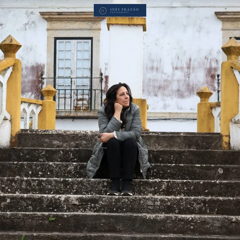 Mulher sentada numa escadaria de pedra diante de uma fachada antiga com pormenores amarelos, fotografia de retrato por Inês Frazão.
