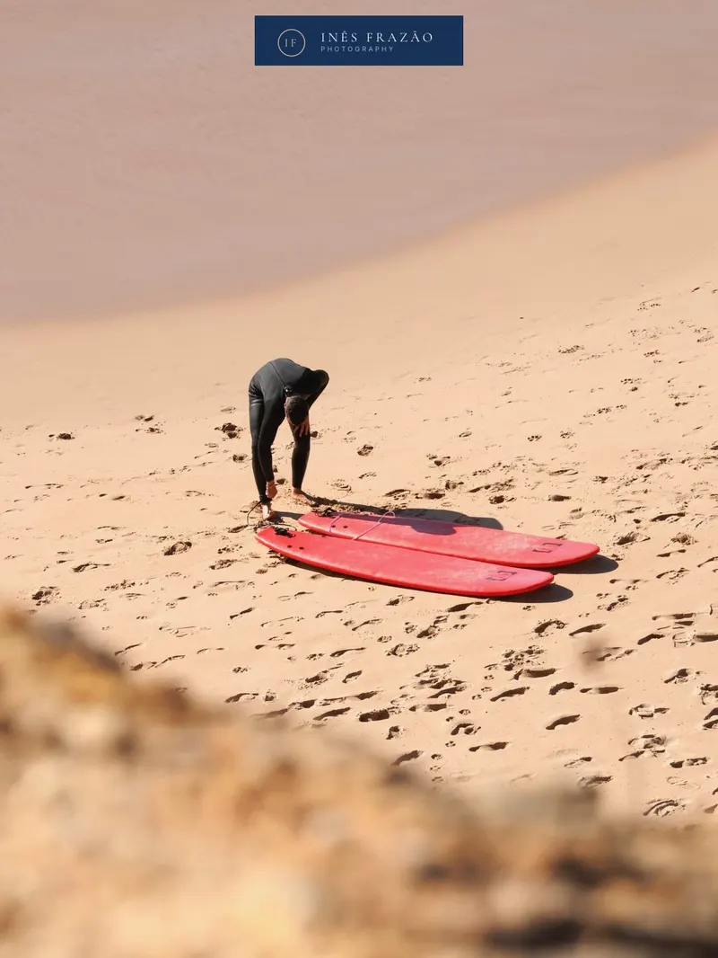 Surfista a preparar a prancha na praia, captado num momento natural e espontâneo antes da sessão. Fotografia documental de desporto por Inês Frazão.