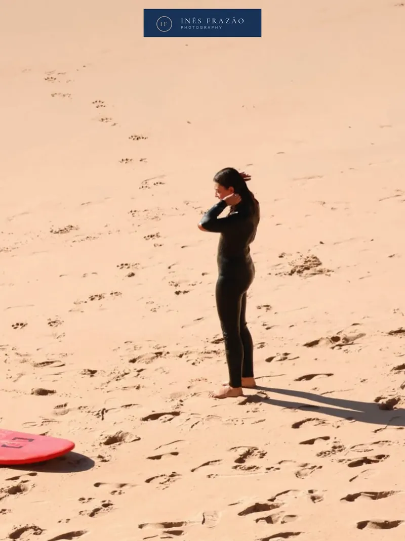 Surfista na areia momentos antes de entrar no mar, numa composição calma que contrasta com a energia das ondas. Fotografia de desporto por Inês Frazão.